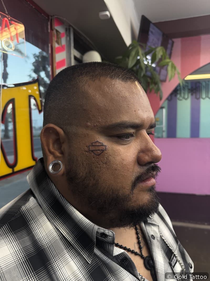 Bar and shield face tattoo by Gia “DOC RI” at Gold Tattoo Vegas